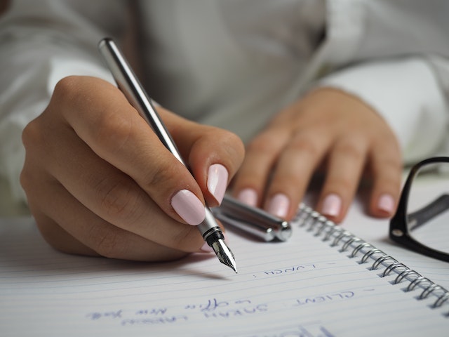 Person with pink nail polish using a fountain pen to write notes